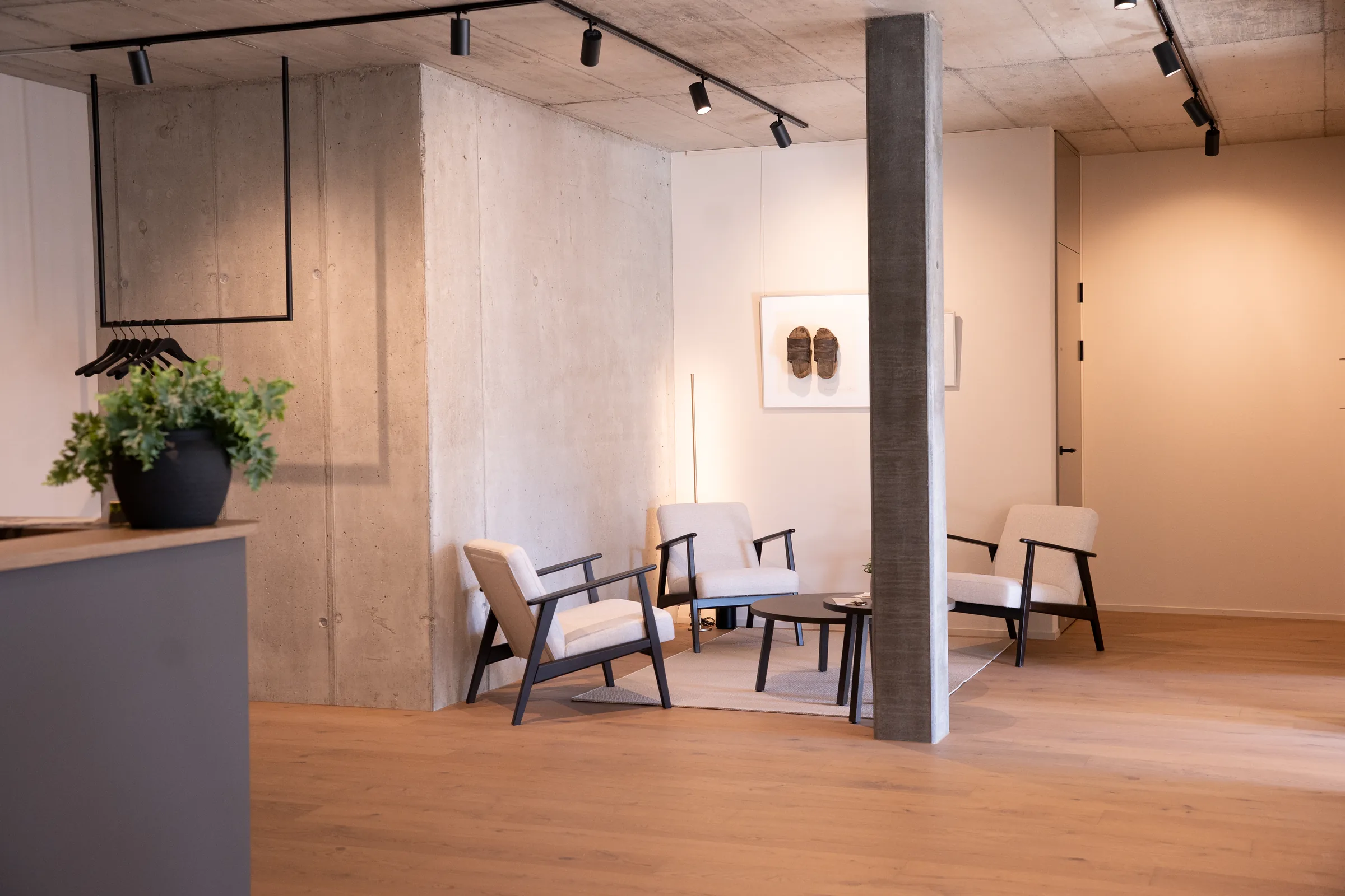 PODORO Podologiepraxis Muri AG – Wartebereich mit Sitzgruppe, Sichtbetonwand und Garderobe